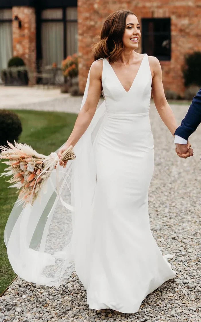 Vestido de novia sencillo de corte trompeta con escote en V, sin mangas, largo hasta el suelo y cola larga en la espalda en V.